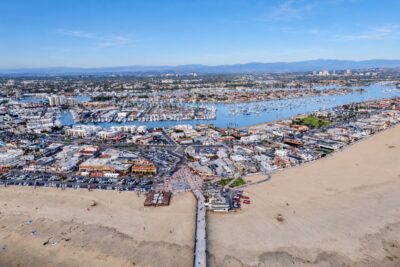 Aerial view of Newport Harbor, waterfront homes and boats beneath a clear blue sky